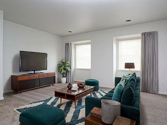 Inviting living room with modern decor, featuring a plush teal sofa, stylish coffee table, and a large flat-screen TV on a sleek wooden cabinet.