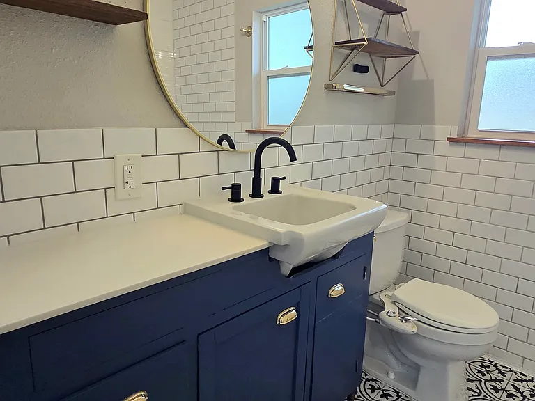 Modern full bathroom offers hand selected tiles, accent vanity, sleek lighting and open shelving in addition to the closet next to the tub.