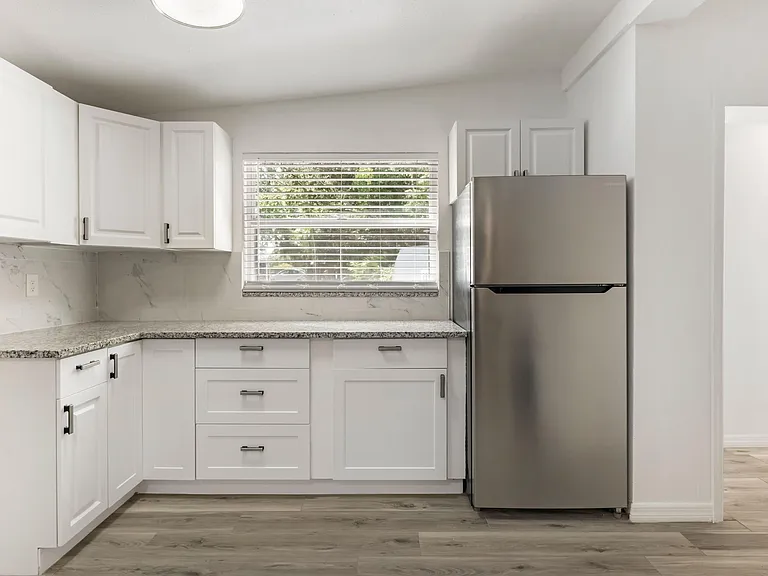 Clean, functional kitchen with ample cabinet storage, stone-look counters, and a full-size refrigerator beside a window.
