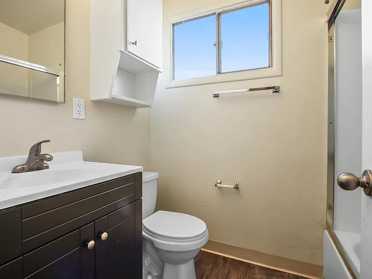 Bathroom with shower and tub combo at the right, single vanity with dark brown wood style cabinet