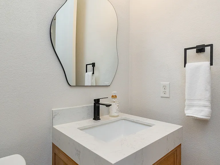 Chic powder room with a unique wavy mirror and modern wood vanity