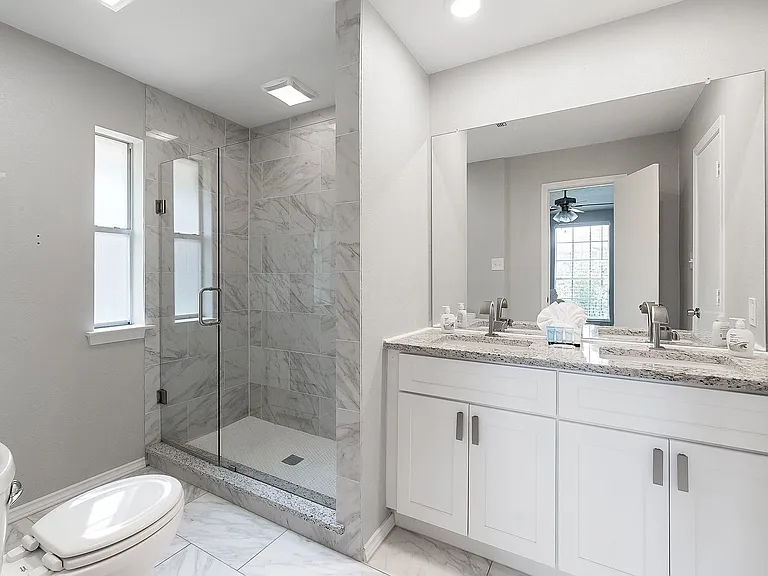 Primary bathroom with marble finish floors, a stall shower, double vanity, and a ceiling fan