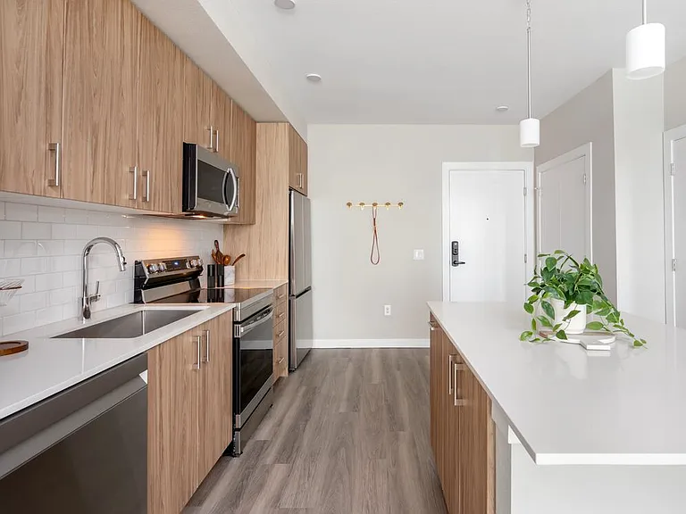 Finish Package II Kitchen with oak cabinetry, white quartz countertops, stainless steel appliances, pendant lighting, and hard-surface vinyl plank flooring