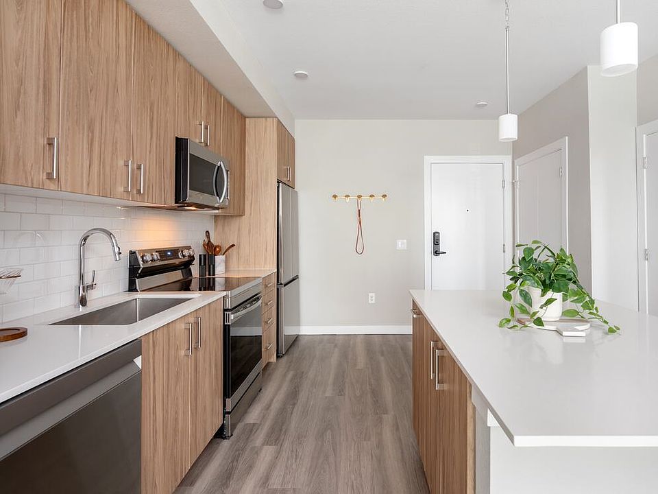 Finish Package II Kitchen with oak cabinetry, white quartz countertops, stainless steel appliances, pendant lighting, and hard-surface vinyl plank flooring