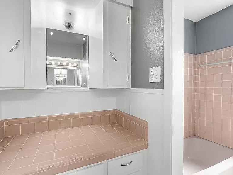 View of dressing area side of Hall Bath with lots of cabinets, mirror, and countertop area for display storage and tub/shower enclosure