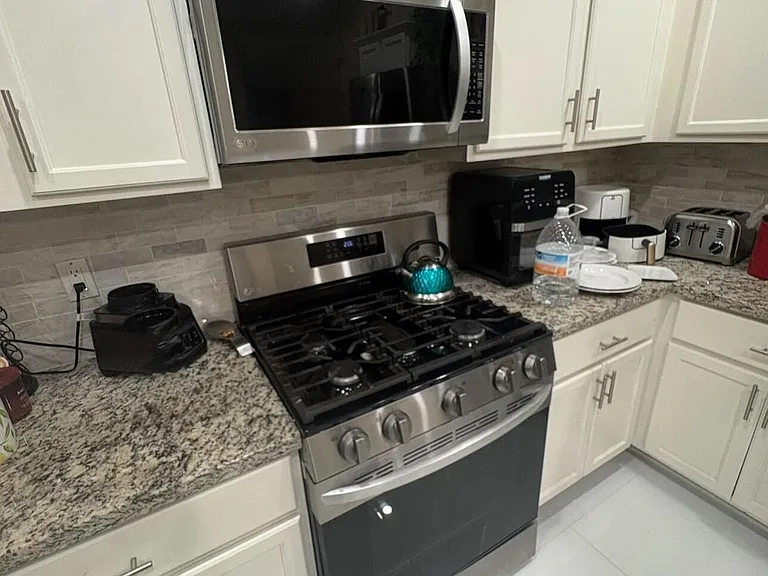 Kitchen with shaker-style cabinetry, granite countertops, tile backsplash, and stainless steel gas range with over-the-range