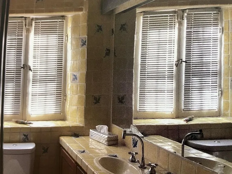 Bathroom has double sink, tub with shower, tilework throughout.
