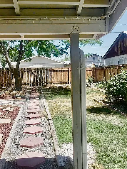 Beautifully landscaped backyard. Walkway from home to gate. Notice grass and mature rose bushes on right. Covered patio. Mature mimosa tree in background.
