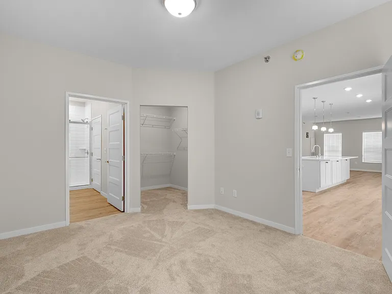 Inviting bedroom featuring plush carpet, connecting to a sleek bathroom, spacious walk-in closet, and open-concept kitchen with modern lighting. Inviting bedroom featuring plush carpet, connecting to a sleek bathroom, spacious walk-in closet, and open-con