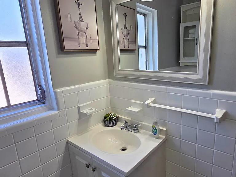 Bright clean bathroom with window, shower, sink, and wall art