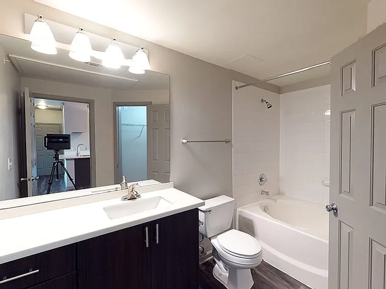 Apartment bathroom with white countertop, dark hardwood cabinets, and dark grey hardwood floors.