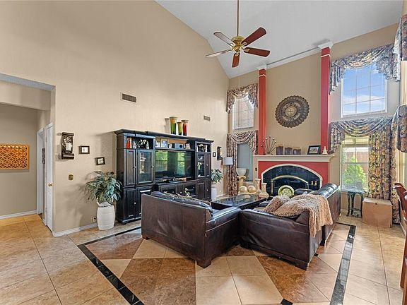 Living room featuring high vaulted ceiling, a ceiling fan, inlaid floor details, and a fireplace