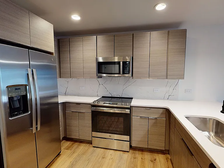 Apartment kitchen with stainless steel appliances, quartz countertops and wood-style flooring.