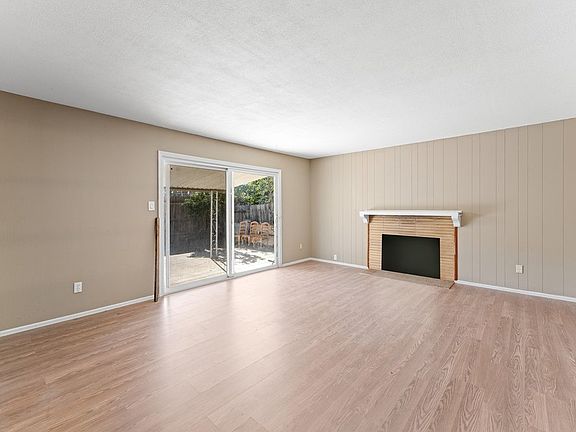 Spacious living room with fresh paint, new flooring, vintage mantle fireplace, and sliding door leading to the backyard.