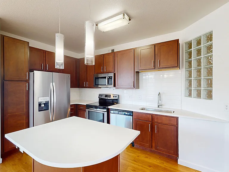 Apartment kitchen with stainless steel appliances, quartz countertops and wood-style flooring.