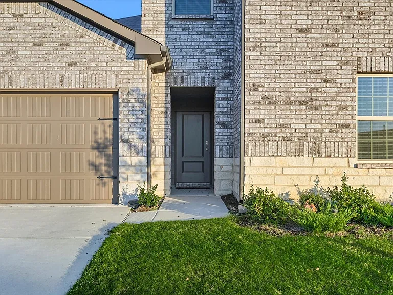 Doorway to property with brick siding, concrete driveway, a garage, and a lawn