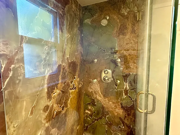 Walk-in shower with polished Onyx stone walls, body sprays and shower head.