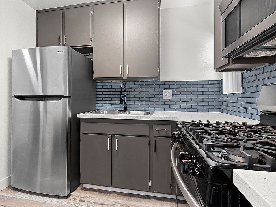 Blue tiled kitchen with stainless steel fridge, oven, and microwave.