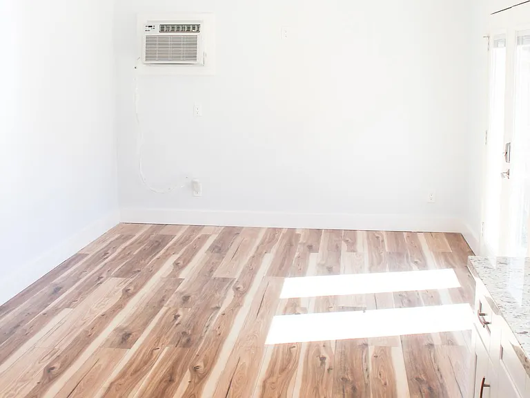 Gorgeous hardwood flooring stands out in the natural lighting and neutral wall colors. Large living area with ceiling fan and window ac/heater unit.