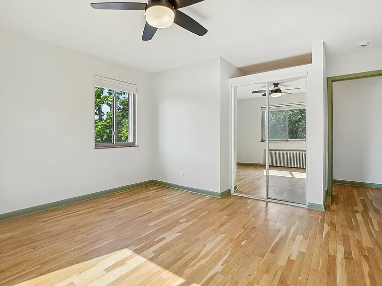 Bright, spacious bedroom with hardwood floors, large window with green views, and mirrored closet doors.