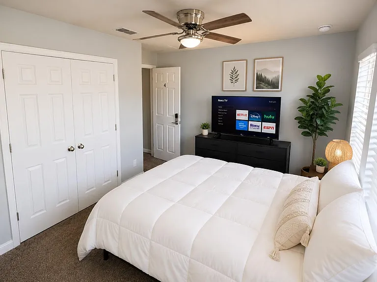 Furnished bedroom with a queen bed, dresser and TV, plus a closet and ceiling fan for everyday comfort.