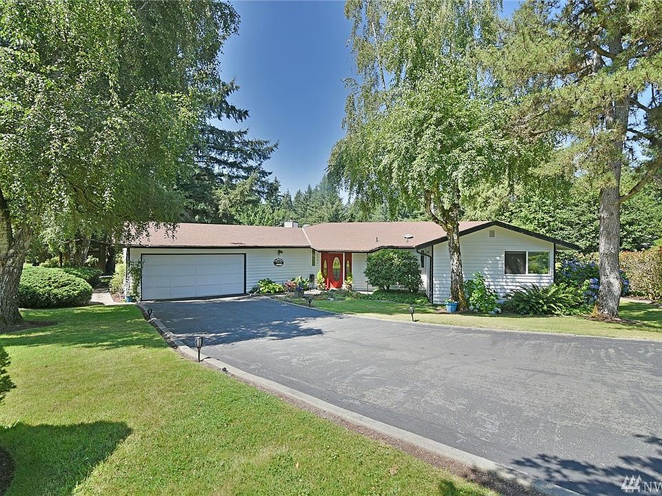 Front of home with mature trees and garden space.