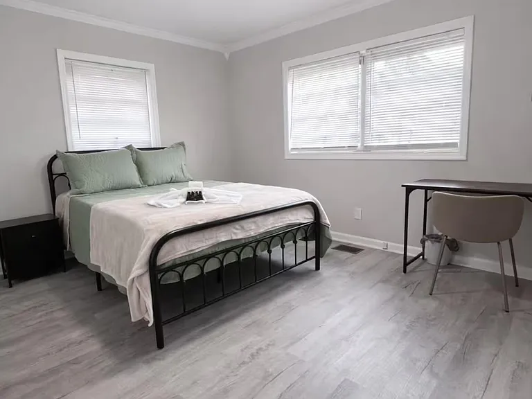 Spacious bedroom with a ceiling fan, two windows with blinds, and hard-surface flooring plus a dedicated desk area.