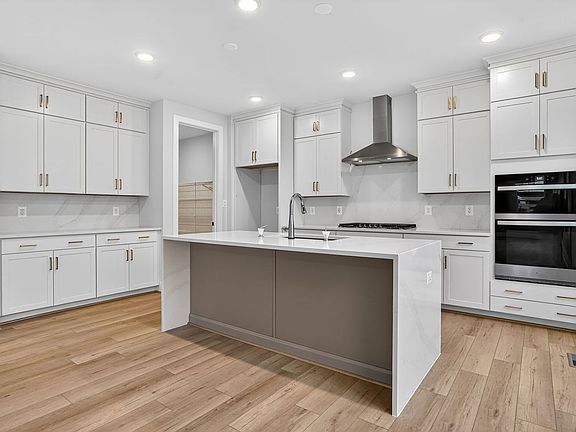 A modern, well-lit kitchen with white cabinets, a central island, and hardwood floors.