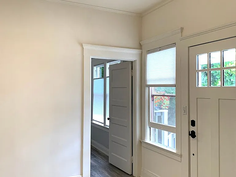 A view of the entrance and living room with a new door, tile flooring, classic moulding, fresh paint, new lighting and blinds.