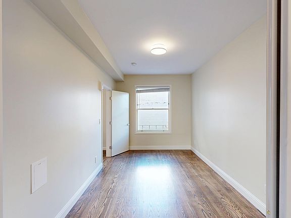 Bright and spacious room with wood flooring, a doorway, and a window letting in natural light