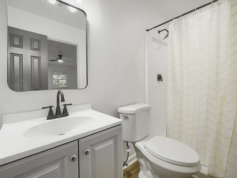 Updated full bath with single-sink vanity, framed mirror, and tub/shower combo with curtain and modern fixtures.