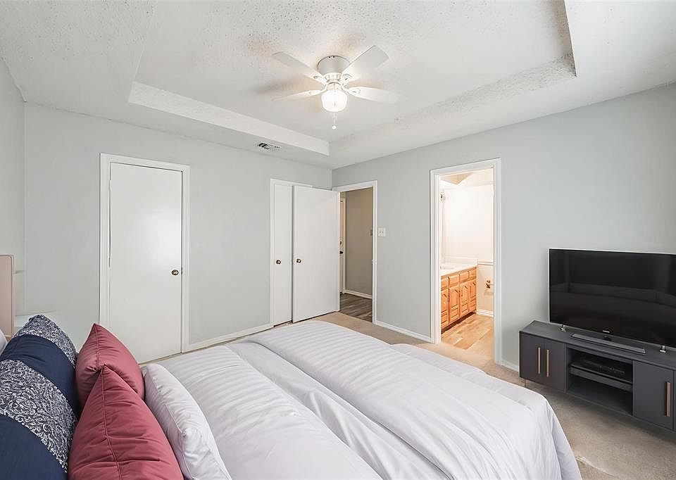 Bedroom featuring a tray ceiling, carpet flooring, a ceiling fan, connected bathroom, and a textured ceiling