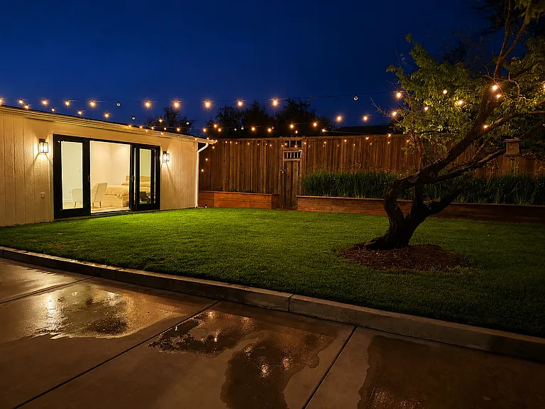 Evening view showcasing the detached studio and beautifully lit backyard