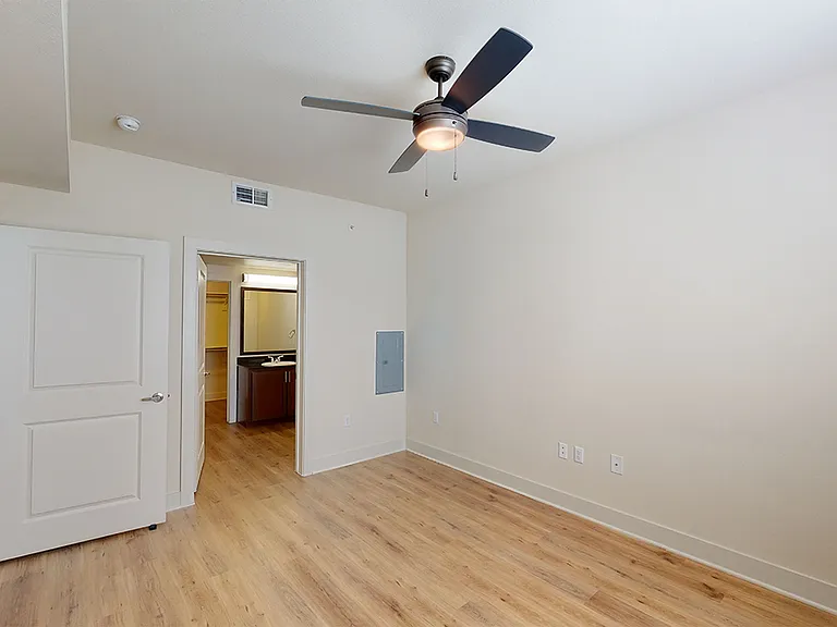 Spacious apartment bedroom with large closet, attached bathroom and wood-style flooring.