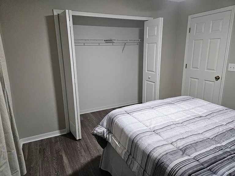 Bedroom with a comfortable bed and a wide closet featuring double doors and a full-length hanging shelf.
