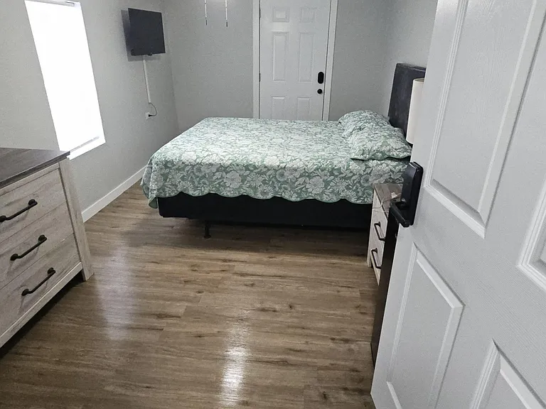 Private bedroom featuring a full bed, dresser storage, and wood-style flooring, plus a wall-mounted TV and window light.