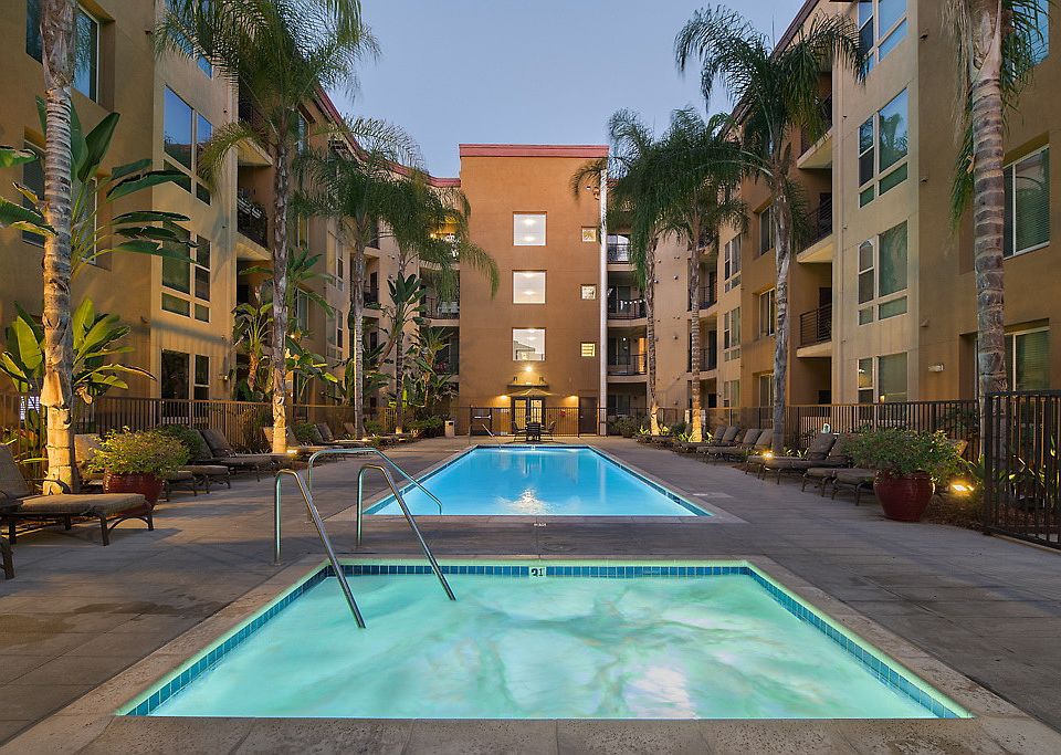 Outdoor spa and swimming pool area with sundeck and lounge seating surrounded by palm trees at dusk.
