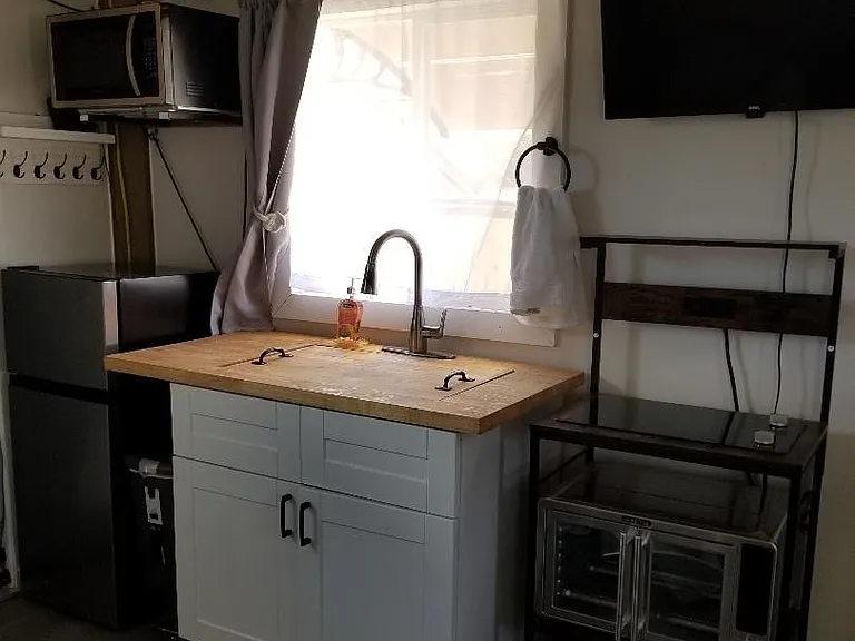Kitchen with fridge, wall mounted microwave, air fryer/convection oven, induction double cooktop, Wall mounted TV, Sink converted to butcherblock countertop, pull down faucet.
