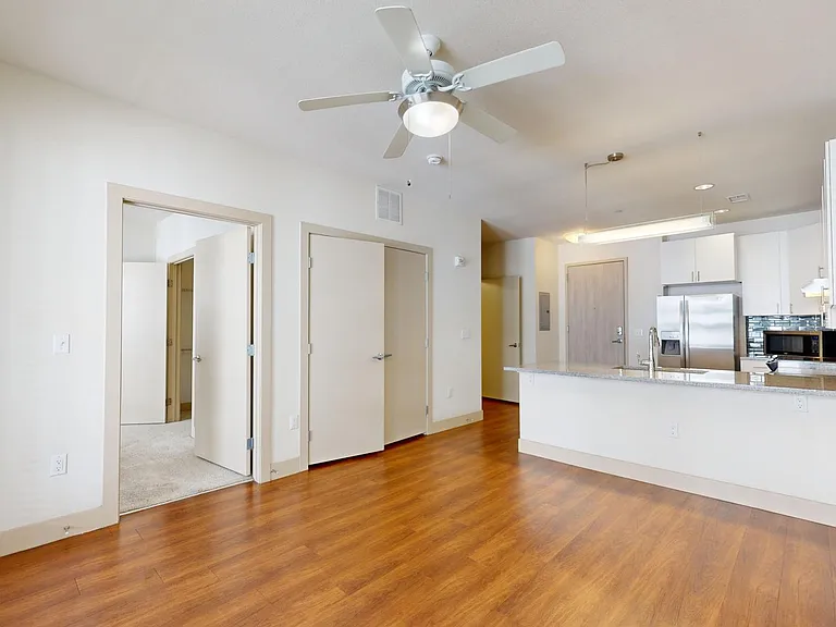Apartment kitchen with stainless steel appliances, dining and living room with wood-style flooring.
