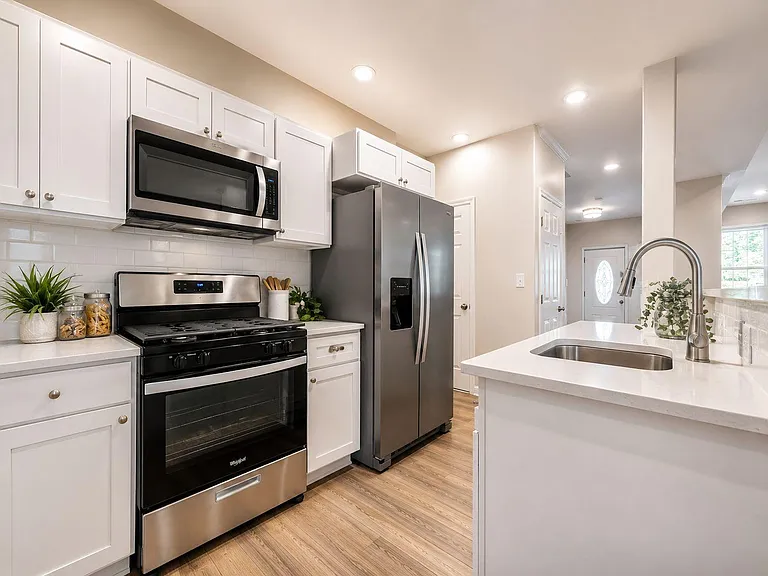 Updated kitchen with white cabinetry, subway-tile backsplash, stainless appliances, and a large island with sink.