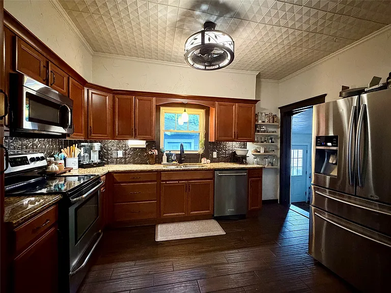 Kitchen featuring dark wood-finish flooring, L-shaped cabinetry with granite-style countertops, stainless steel appliances, a decorative ceiling with a central light fixture, and a window above the sink