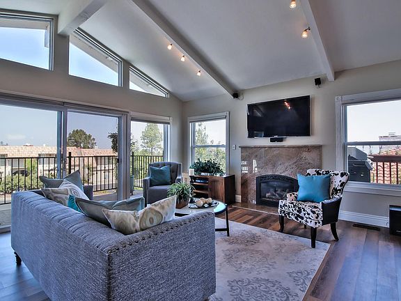 Family room with gas fireplace in the granite surround. The 55" HDTV is wall mounted with surround sound built in speakers. Wooden floors and a deck facing the Los Gatos Mountains. There is a granite desk next to the 3 wall mounted bookshelves.