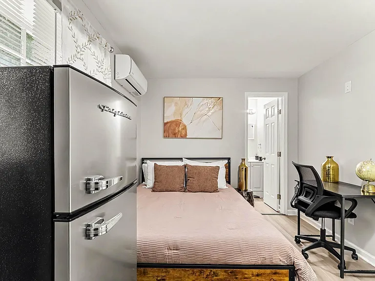 Furnished bedroom with a full bed, dedicated desk workspace, and in-room mini fridge, plus quick access to the bathroom.
