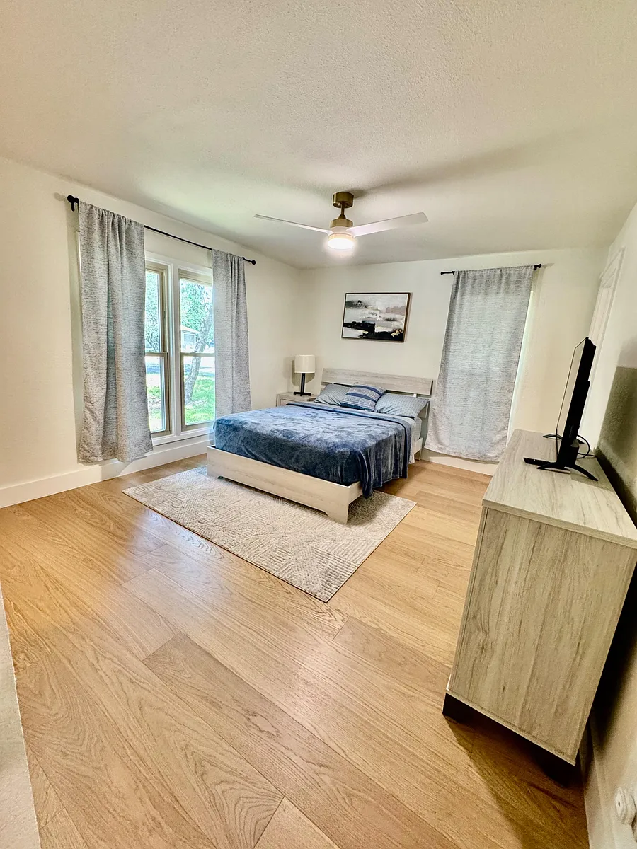 Photo 2 of 9 - Mossbrook Cv - Austin, TX Spacious bedroom with a ceiling fan, large windows with drapes, and room for a dresser or TV setup. - Mossbrook Cv
