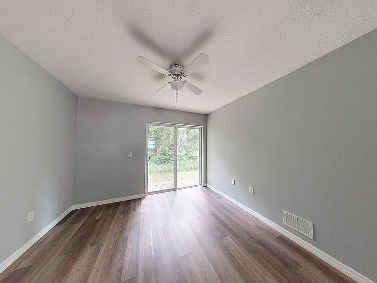 Bright, spacious room with elegant wood flooring, modern ceiling fan, and large glass doors opening to a serene outdoor view.
