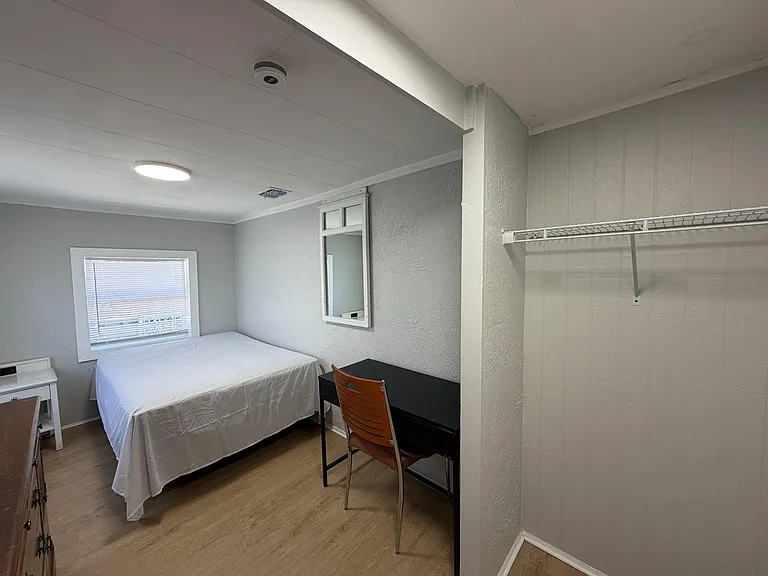 Private bedroom with a bed, work desk, and window with blinds, plus a wall shelf for added storage.