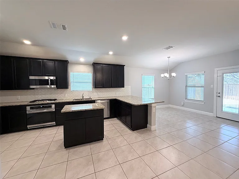 Kitchen featuring dark cabinetry, stainless steel appliances, a center island, light-toned countertops, and tile flooring