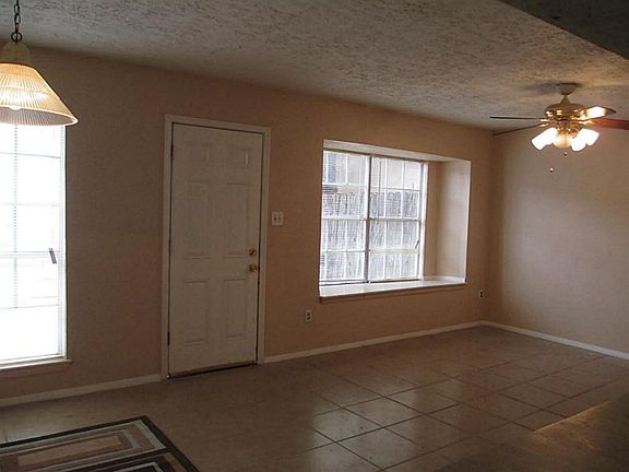 View of dining room and living room. Room has large windows, new tiles and fresh paint. Door leads t