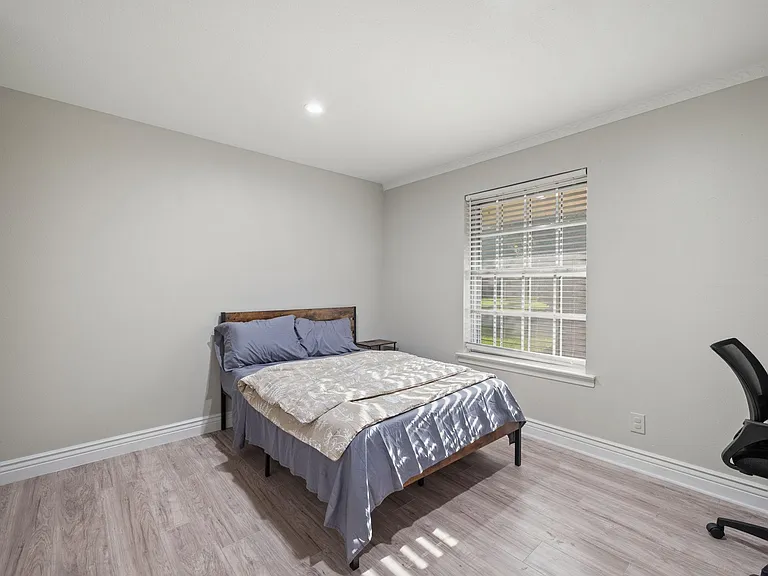 Bedroom with a full bed, wood-look flooring, and a large window with blinds for natural light and privacy.