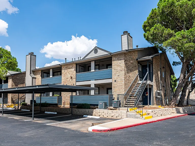 The exterior of an apartment building is shown with covered parking in front.